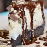 Slice of Andes Mint Cheesecake topped with mint leaves and chocolate drizzle