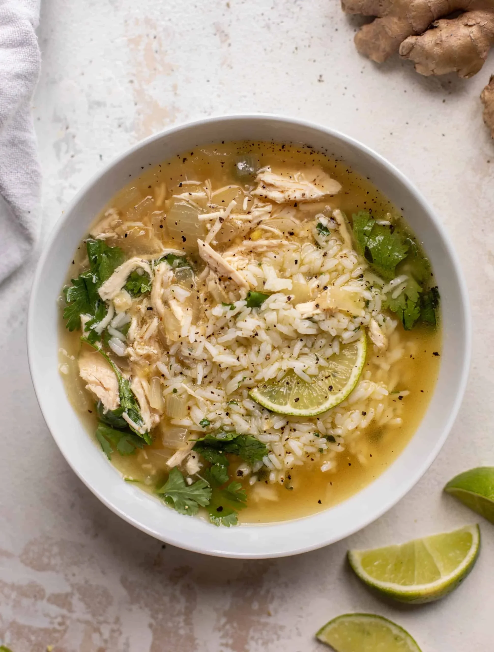 Bowl of ginger lime chicken and rice soup garnished with herbs and lime slices