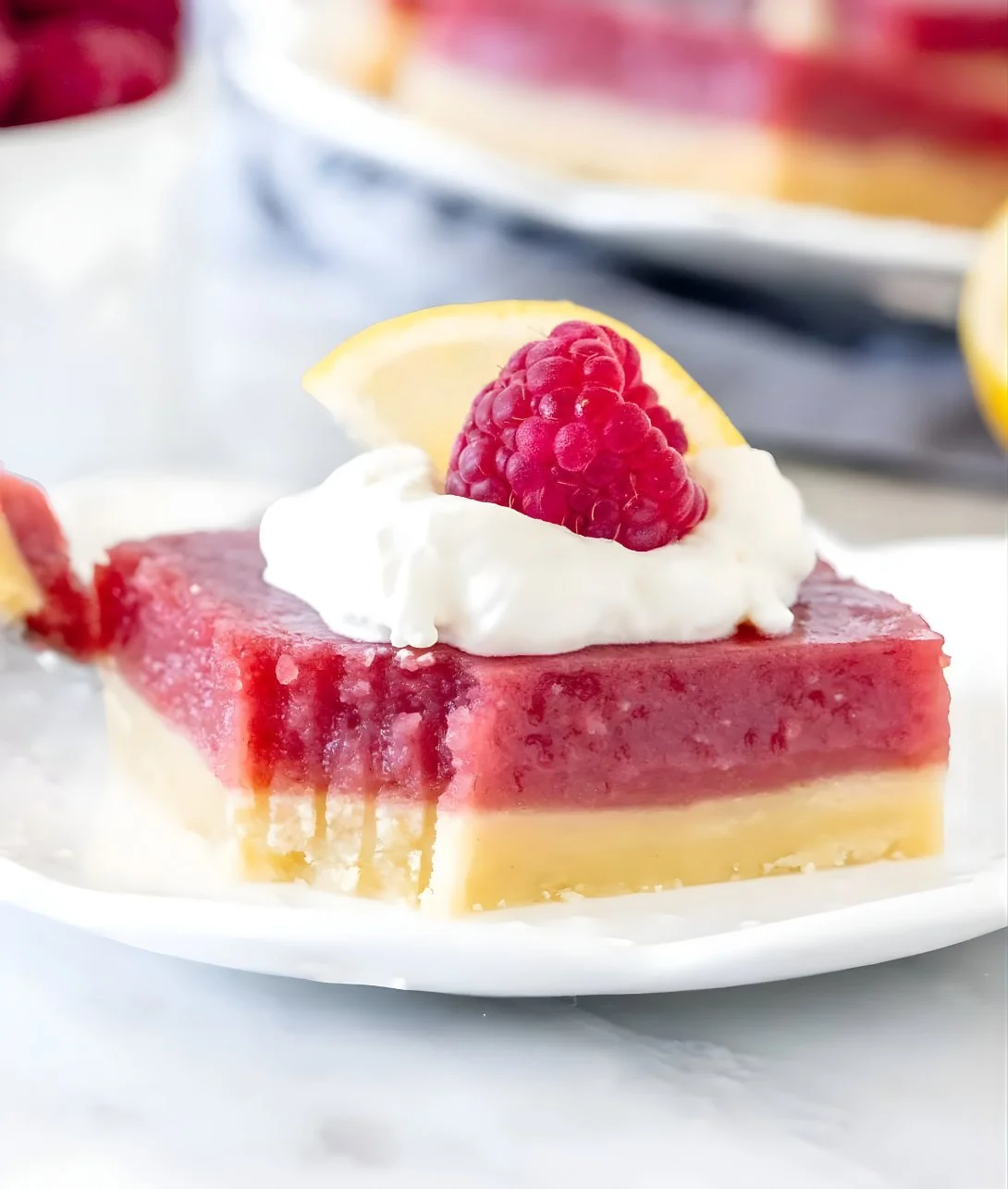 Delicious lemon raspberry bars on a plate garnished with fresh berries.