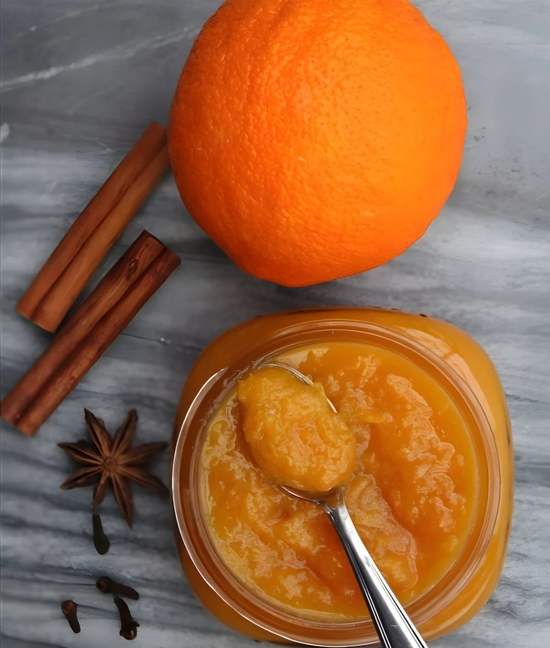 Orange jam with warm spices in a jar with a spoon