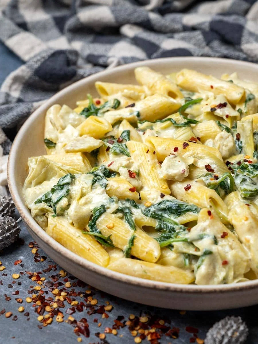 Creamy spinach artichoke pasta served in a bowl, garnished with herbs.