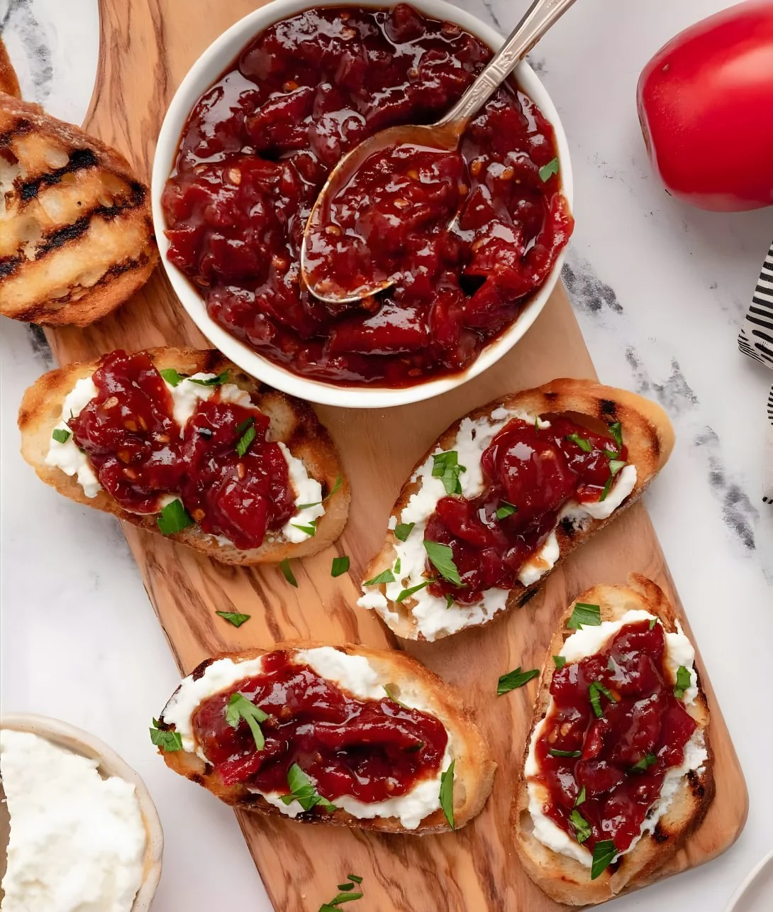 Homemade tomato jam spread on toast with fresh tomatoes.