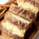 Slice of cinnamon sugar donut bread topped with sugar on a wooden cutting board