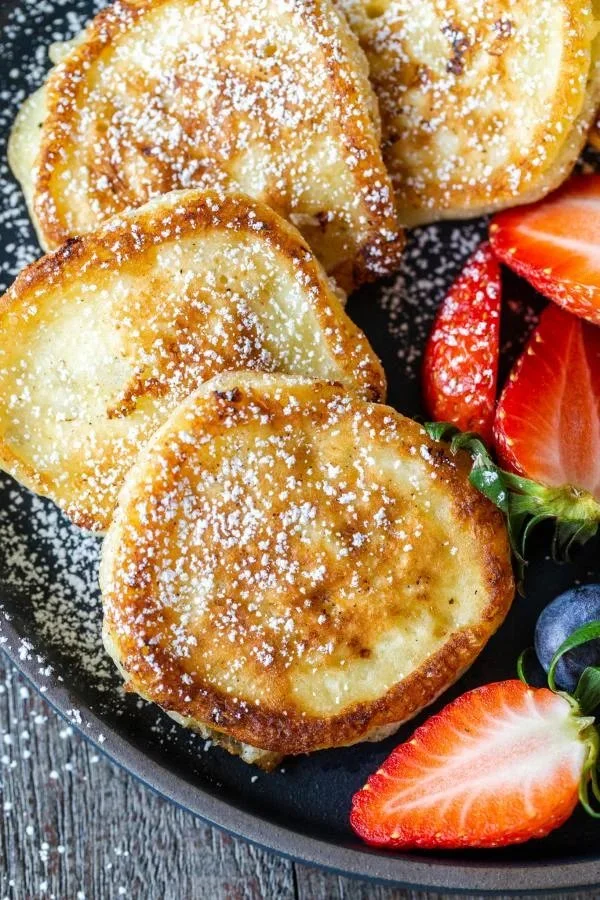 Fluffy cottage cheese pancakes served with fruits and syrup on a plate