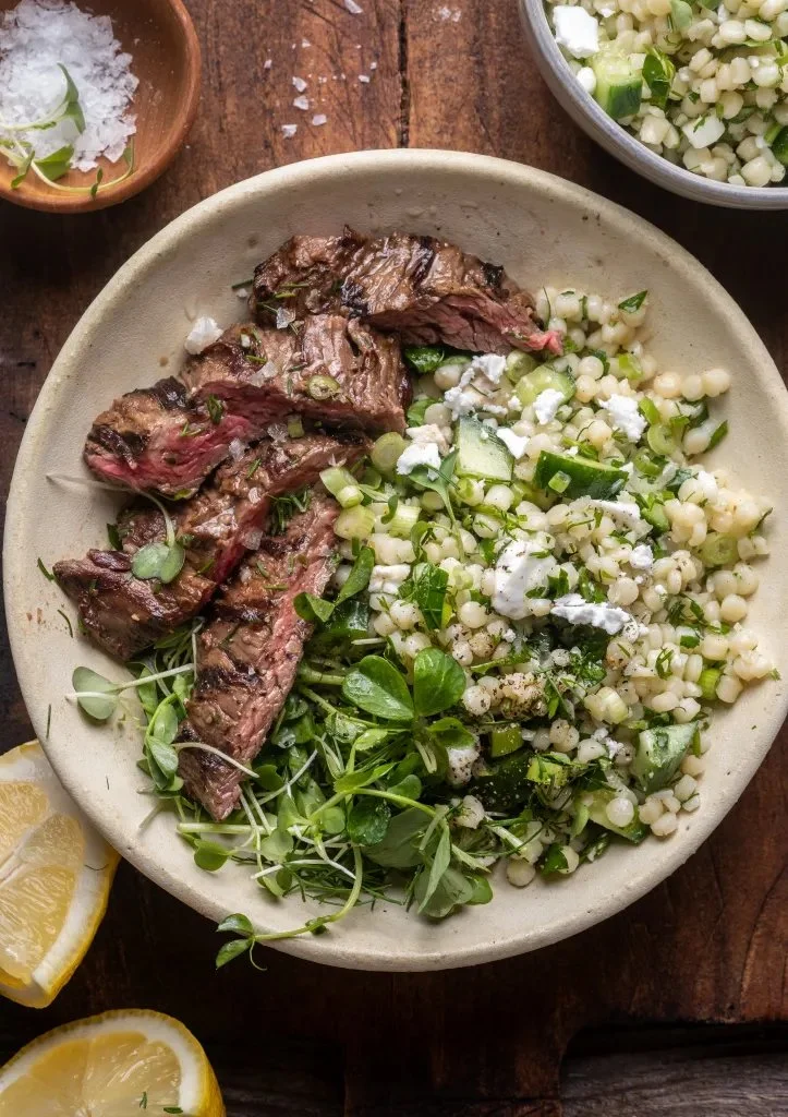 Grilled skirt steak served with lemon herb couscous salad on a plate.