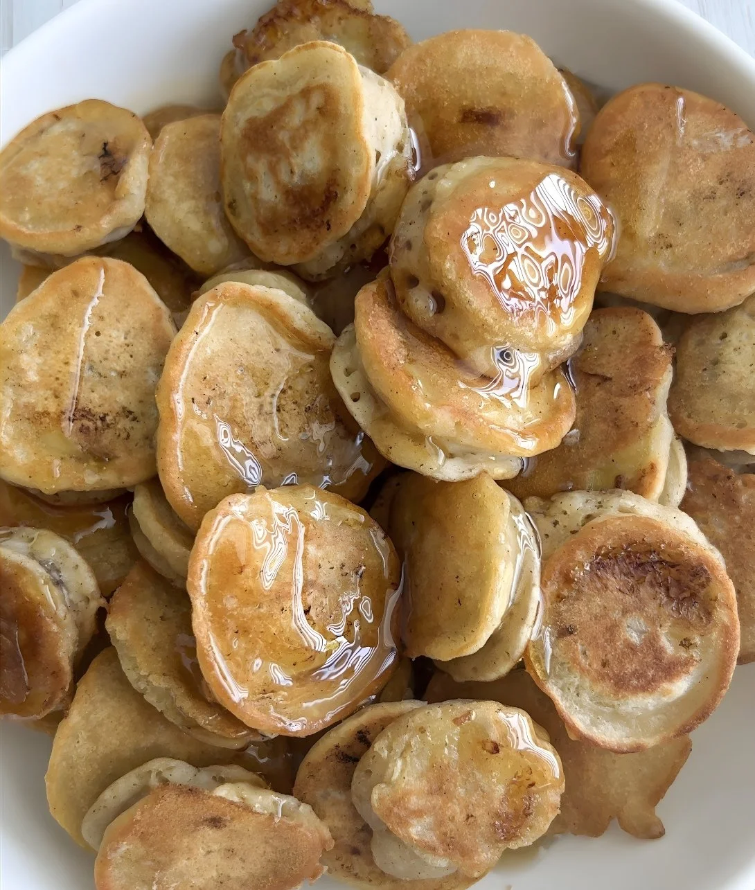 Mini Banana Pancake Bites served on a plate, topped with banana slices and syrup.