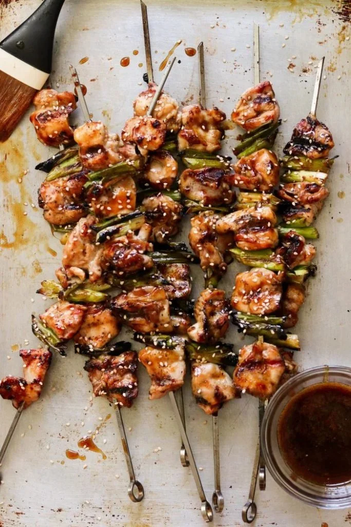 Paleo chicken skewers grilling on barbecue with herbs and spices.