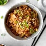 Bowl of spicy peanut butter noodles topped with vegetables and herbs