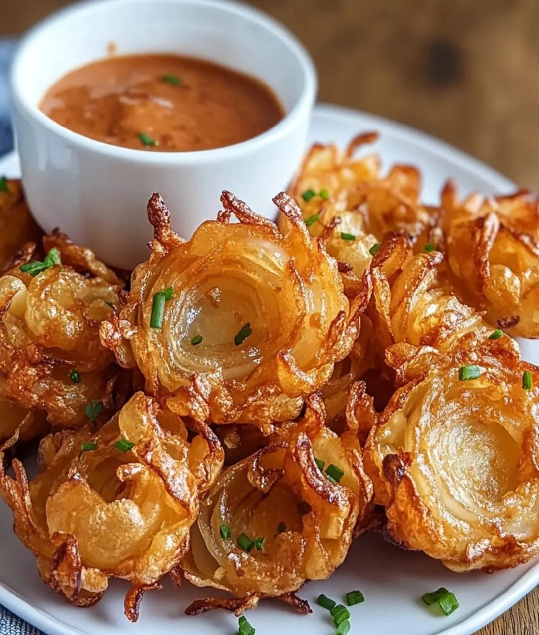 Crispy mini blooming onions cooked in an air fryer, served with dipping sauce.