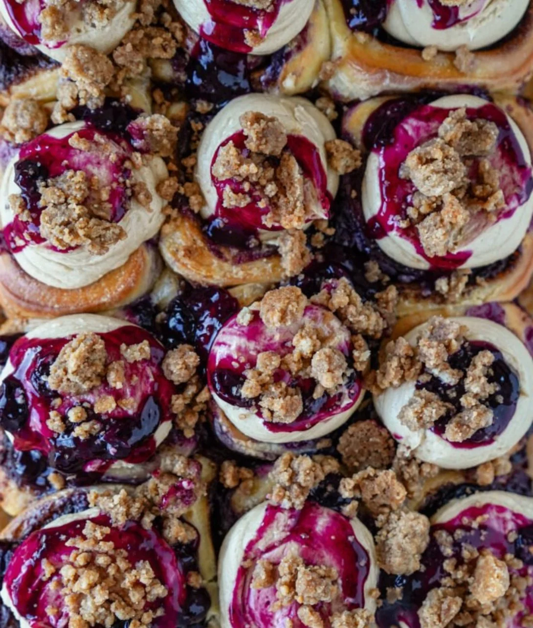 Freshly baked blueberry cinnamon rolls drizzled with icing on a plate