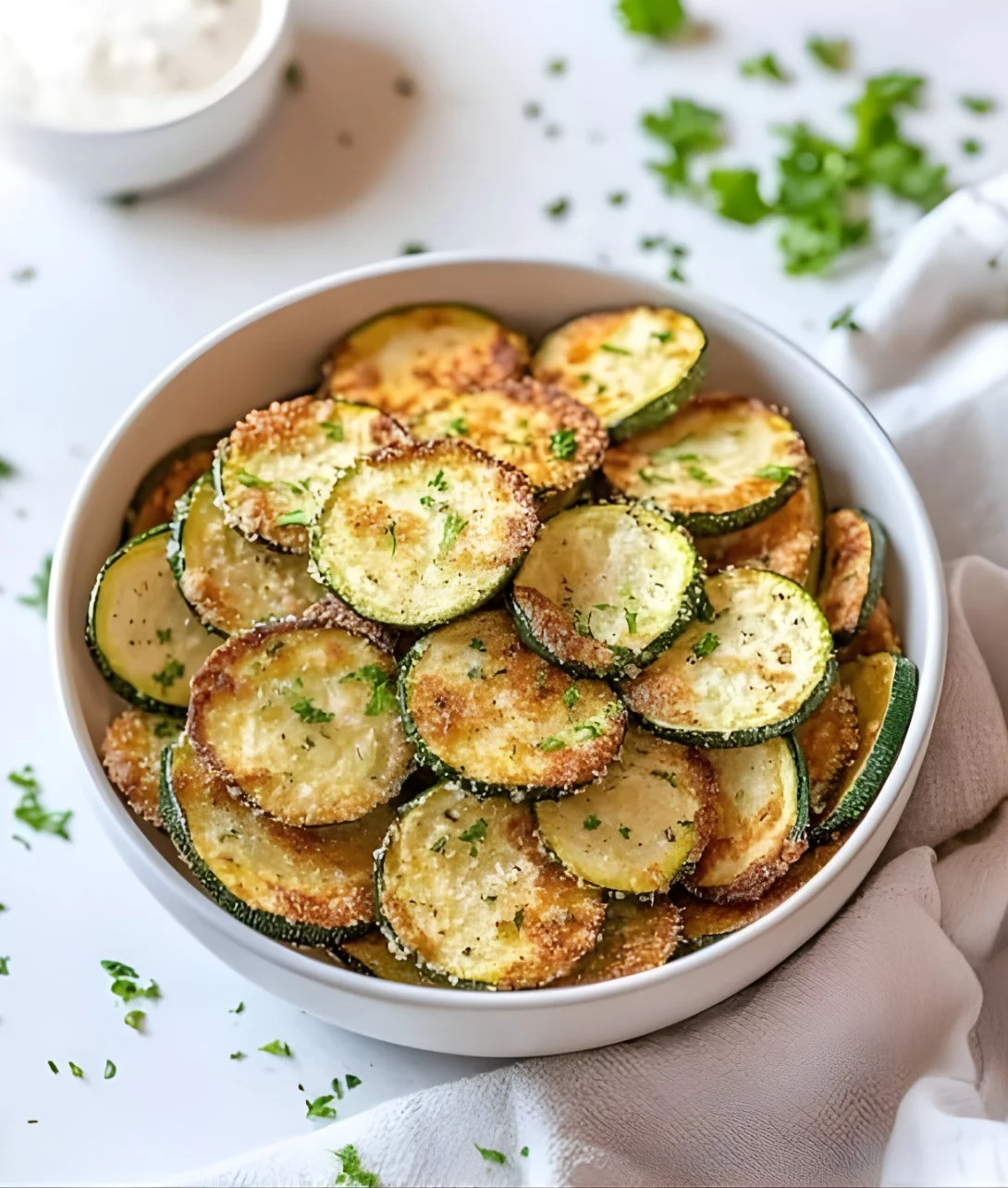 Homemade crispy zucchini chips with seasoning on a plate.