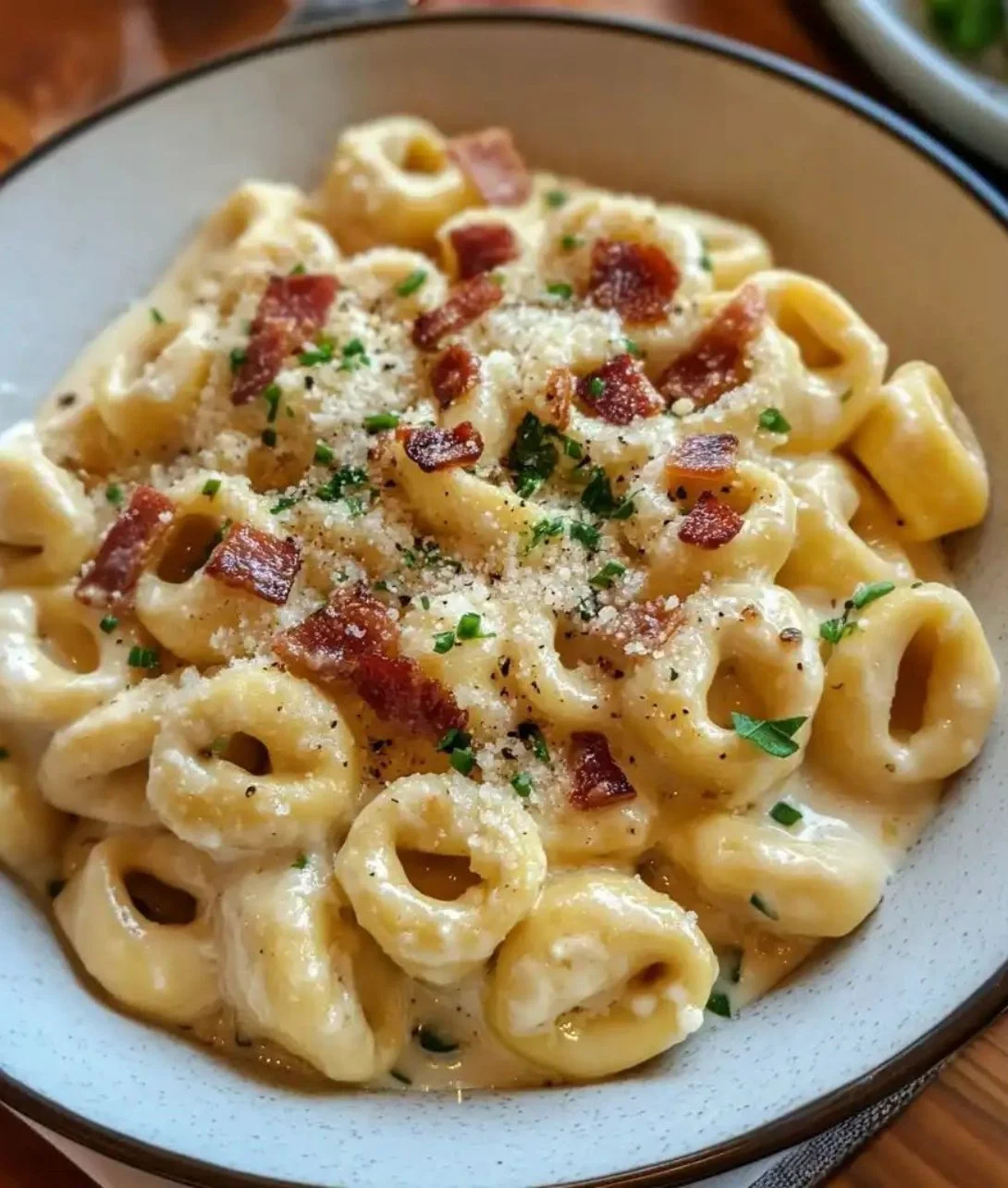 Bowl of creamy tortellini carbonara topped with parmesan and herbs