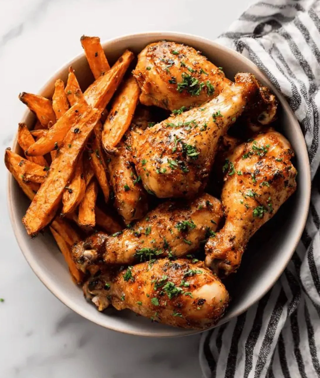 Baked chicken drumsticks served with sweet potato fries on a plate.