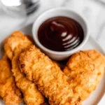 Crispy air fryer chicken tenders served on a plate with dipping sauce.