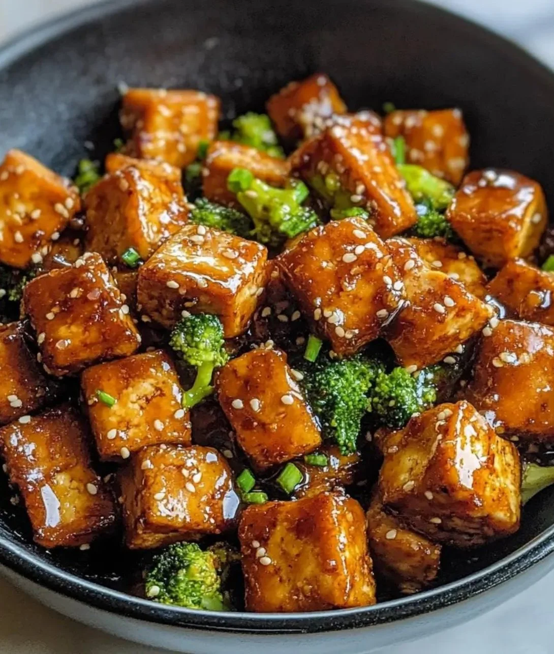 Plate of crispy honey garlic tofu garnished with sesame seeds and green onions.