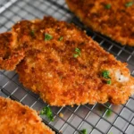 Crispy panko crusted chicken breasts on a plate, garnished with herbs.