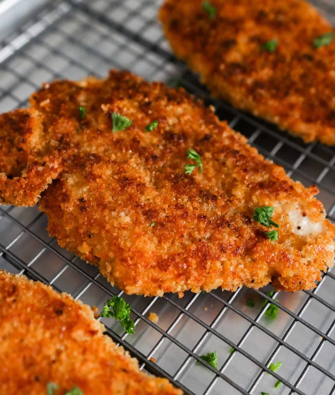 Crispy panko crusted chicken breasts on a plate, garnished with herbs.