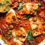 Plate of Fish Puttanesca featuring fish, tomatoes, olives, and herbs.