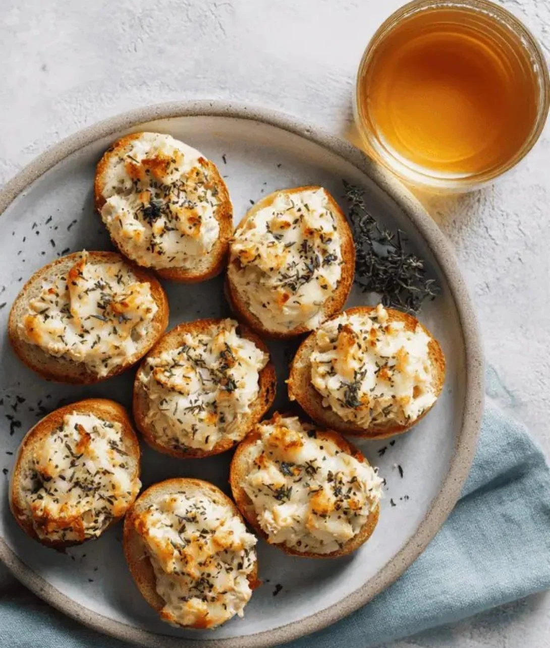 Mini tuna melts served on a plate with melted cheese and fresh herbs
