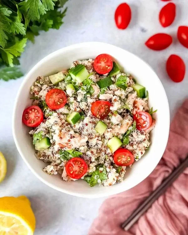 Bowl of healthy Salmon Quinoa Salad with colorful vegetables and dressing.