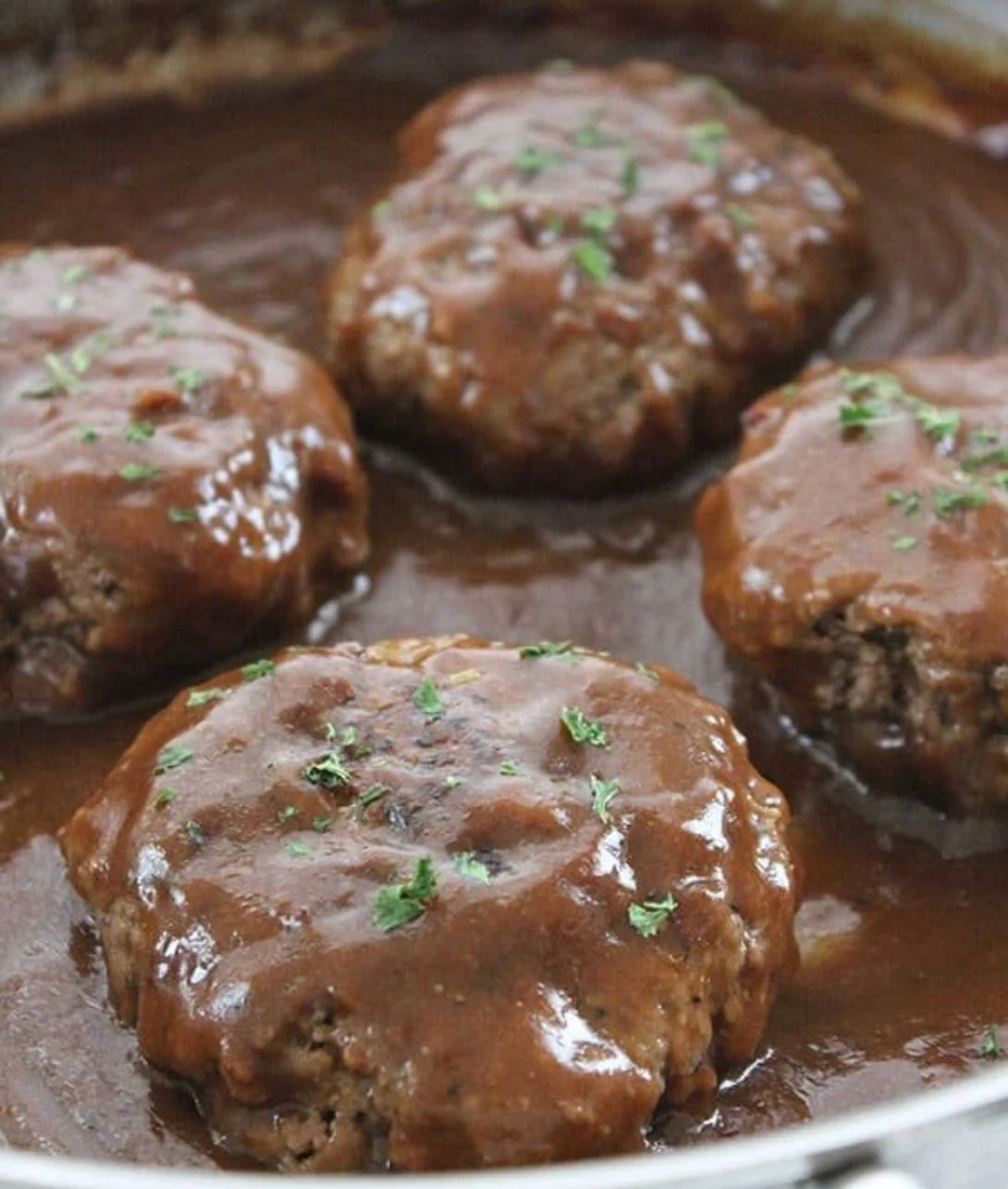A plate of homemade simple Salisbury steak served with gravy and vegetables.