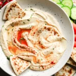 A bowl of creamy hummus garnished with olive oil and parsley, served with pita bread.