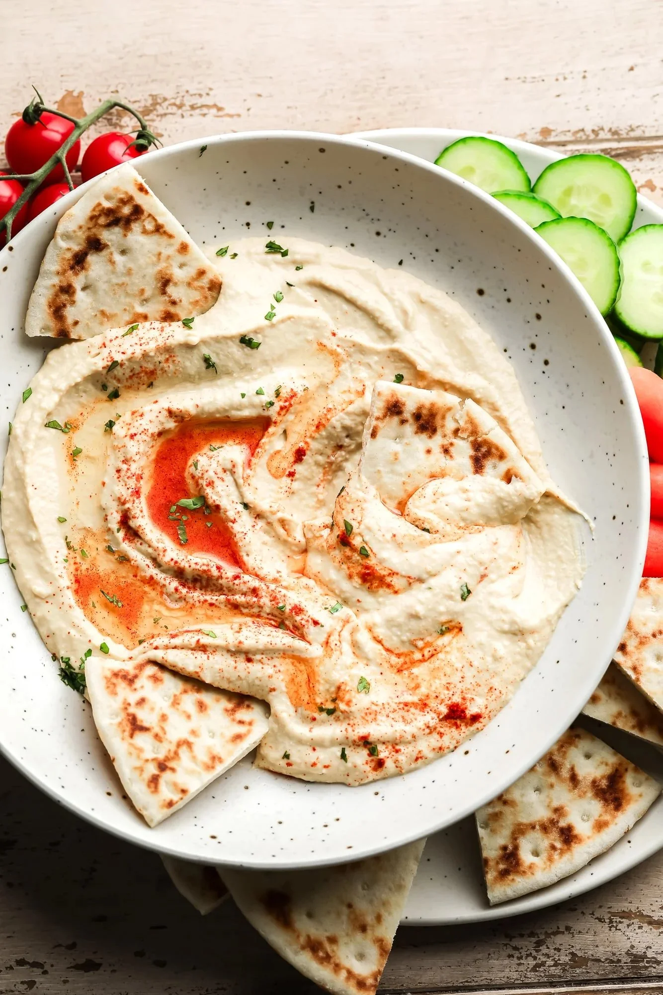 A bowl of creamy hummus garnished with olive oil and parsley, served with pita bread.