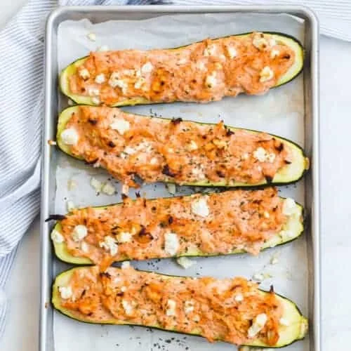 Buffalo chicken zucchini boats topped with cheese and served on a plate