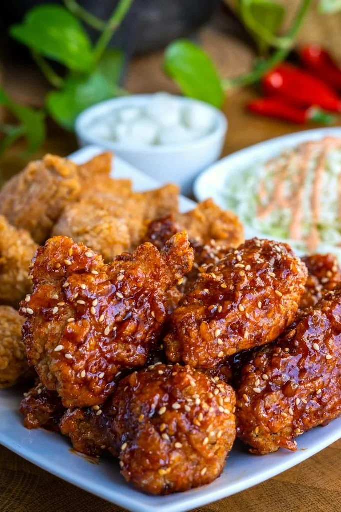 Plate of crispy Korean-style fried chicken garnished with sesame seeds and scallions.