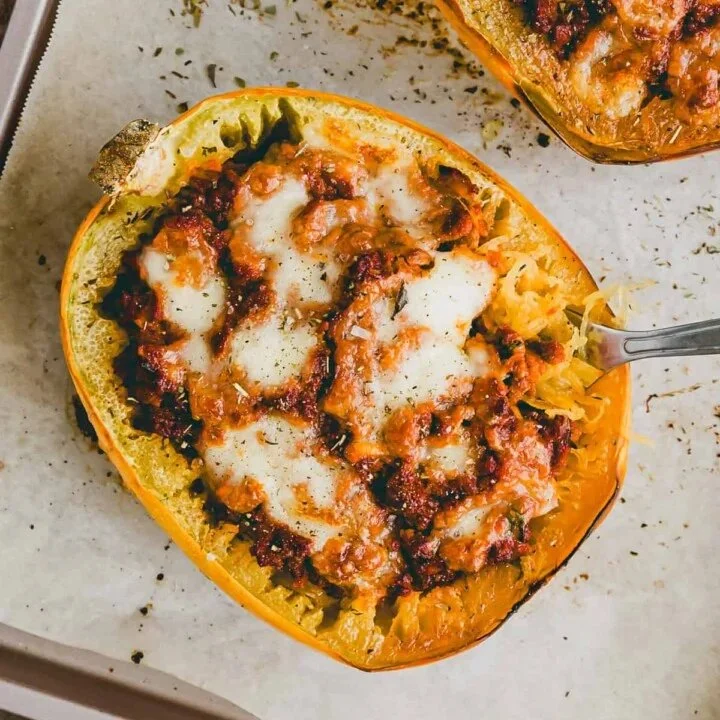 Filled spaghetti squash topped with vegetables and herbs on a plate