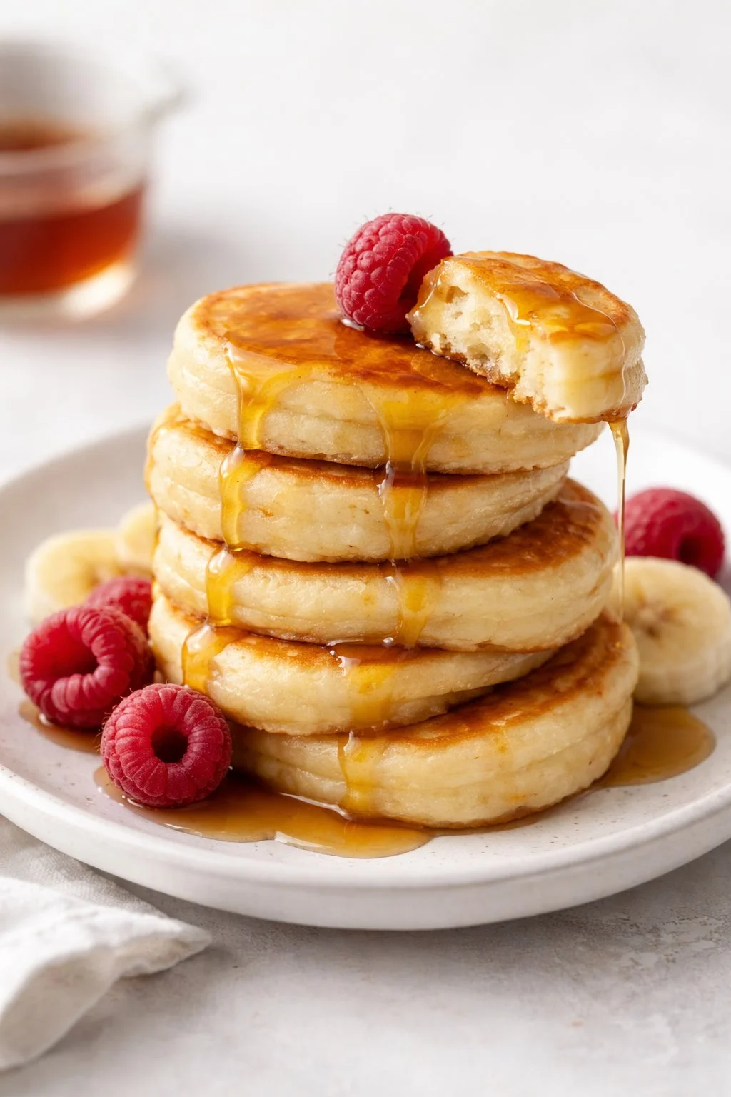 Fluffy banana pancake minis stacked on a plate with syrup and fresh bananas