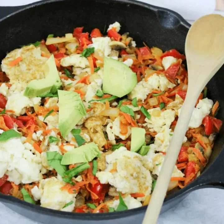 Healthy scrambled eggs with vegetables on a plate garnished with fresh herbs.