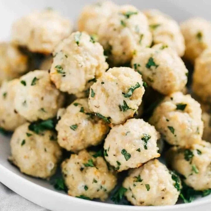 Oven-baked turkey meatballs served on a plate with marinara sauce and herbs.