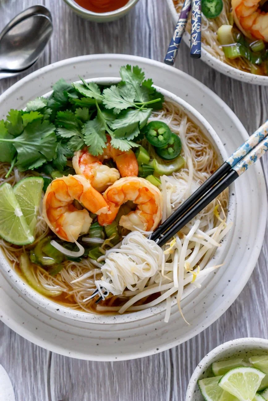 Bowl of Shrimp Pho noodle soup garnished with herbs and lime.